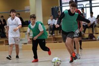 Mehrere Jungs laufen in einer Halle zu einem Fußball. Ein Junge will ihn gleich spielen