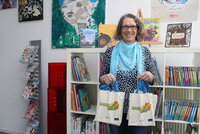 Büchereileiterin Anja Stark steht vor einem Bücherregal und hat Taschen mit Lesestart-Sets in der Hand.