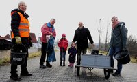 Auch in Erfelden wurde im letzten Jahr eifrig von Groß und Klein gesammelt. Erwachsene und Kinder stehen auf dem Damm in Erfelden. Sie haben Mülltüten, Eimer und Greifzangen zum Einsammeln in der Hand. Außerdem haben sie einen Handkarren dabei.