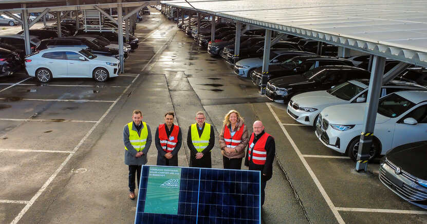 Simon Bartsch (Leiter Logistik Niederlassungen), 1. Kreisbeigeordneter Adil Oyan, Wolfgang Ketterle (Chief Operations Officer), MdL Ines Claus und Bürgermeister Marcus Kretschmann (v.li.) bei der feierlichen Eröffnung Simon Bartsch (Leiter Logistik Niederlassungen), 1. Kreisbeigeordneter Adil Oyan, Wolfgang Ketterle (Chief Operations Officer), MdL Ines Claus und Bürgermeister Marcus Kretschmann (v.li.) stehen zwischen langen Reihen von überdachten Parkplätzen. Auf den Dächern befinden sich lauter Solarplatten.