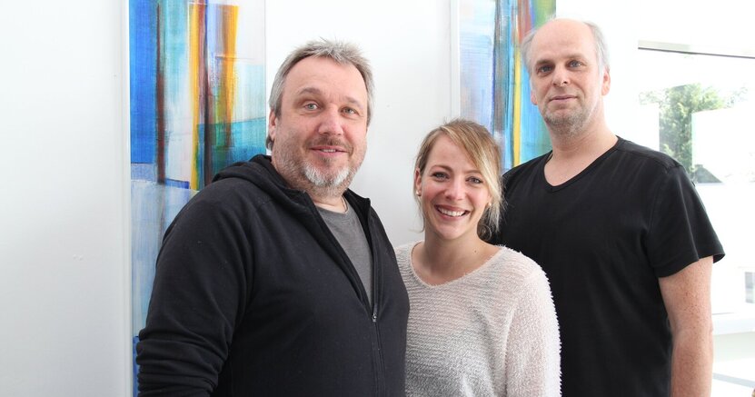 Kai Faßnacht, Julia Spitzer und Heiko Wambold (v.li.) vom Jugendbüro stehen vor einer weißen Wand mit buntem Wandbehang.