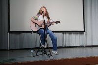 Liedermacherin Sabine Perl sitzt mit Gitarre auf der Bühne.