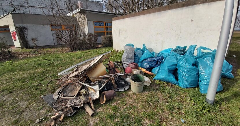 Viele prall gefüllte blaue Müllsäcke sowie verschmutzte Metallteile, zerbrochene Keramik und vieles mehr liegen auf einer Wiese vor einer Mauer. Sie wurden bei einer früheren Müllsammelaktion am Erfelder Altrheinufer gefunden.