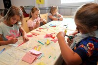 Basteln wie hier 2025 in Leeheim gehört auch zu den Angeboten der Ferienspiele. Kinder sitzen an beiden Seiten eines langen Tisches und malen und schneiden aus.