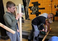 Mit Hilfe von Kai Faßnacht schneidet ein Junge ein Brett zurecht. Weitere Jungen warten mit ihren Brettern.