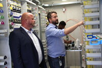 Bürgermeister Marcus Kretschmann und Florian Frommherz von der Deutschen Glasfaser stehen im Hauptverteiler für Crumstadt. Das ist ein Raum, in dem viele Kabel und Schalter zu sehen sind.