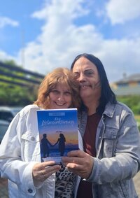 Steffi und Oliver Pletz mit dem Buch „Eine Liebeserklärung an das Leben“ Steffi und Oliver Pletz stehen draußen auf einem Platz. Im Hintergrund ist Grün und der Himmel zu sehen. Sie halten das Buch "Eine Liebeserklärung an das Leben" in den Händen.