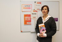 Die Riedstädter Frauenbeauftragte Jennifer Muth steht vor einer Tafel mit Plakaten für das Hilfstelefon. In der Hand hält sie Broschüren mit weiteren Hilfsangeboten.