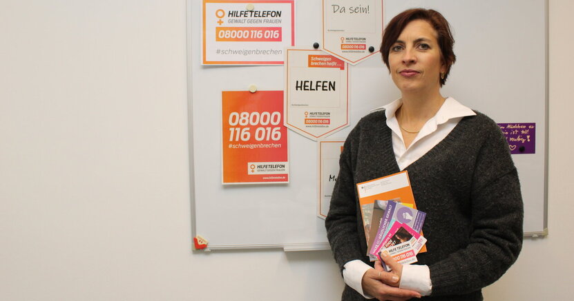 Die Riedstädter Frauenbeauftragte Jennifer Muth steht vor einer Tafel mit Plakaten für das Hilfstelefon. In der Hand hält sie Broschüren mit weiteren Hilfsangeboten.