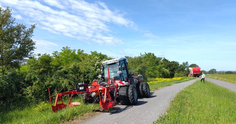 Ein großer Mähtraktor mäht seitlich von einem Deichweg Pflanzen ab.
