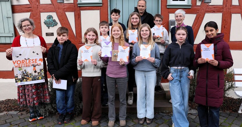 Die Teilnehmerinnen und Teilnehmer des Vorlesewettbewerbs stehen vor dem Büchnerhaus. Mit dabei auch die Juroren Lucia Bornhofen (links), Christian Suhr und Birgit Weinmann. Die Kinder halten Teilnahmeurkunden in den Händen, Lucia Bornhofen ein Plakat mit der Aufschrift "Vorlesewettbewerb".