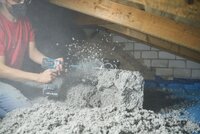 Zu sehen sind Dämmarbeiten auf einem Dachboden. Dabei wird das Dämmmaterial aus Altpapier zerkleinert.