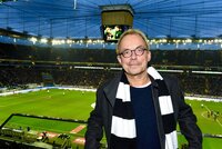 Henni Nachtsheim steht mit schwarz-weißen Fan-Schal im Fußballstadion. Im Hintergrund ist das Spielfeld zu sehen.
