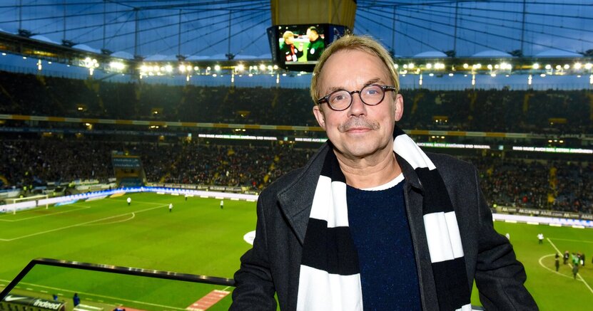 Henni Nachtsheim steht mit schwarz-weißen Fan-Schal im Fußballstadion. Im Hintergrund ist das Spielfeld zu sehen.