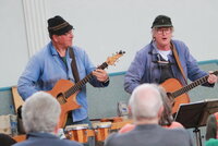 Franz Offenbecher und Klaus Lohr (v.li.) bei einem früheren Auftritt in der TV Halle Erfelden. Franz Offenbecher und Klaus (v.li.) stehen mit ihren Gitarren vor ihrem Publikum. Von den Zuhörerinnen und Zuhörern sind einige Hinterköpfe zu sehen.