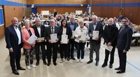 Bürgermeister Marcus Kretschmann und Stadtverordnetenvorsteher Guido Funk stehen mit den neu gewählten Magistratsmitgliedern in einer langen Reihe in der Christoph-Bär-Halle. Die Magistratsmitglieder halten ihre Ernennungsurkunden in den Händen. Hinter ihnen sitzen die Stadtverordneten an ihren Tischen.