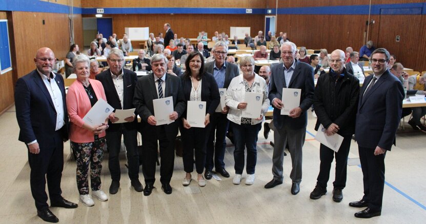 Bürgermeister Marcus Kretschmann und Stadtverordnetenvorsteher Guido Funk stehen mit den neu gewählten Magistratsmitgliedern in einer langen Reihe in der Christoph-Bär-Halle. Die Magistratsmitglieder halten ihre Ernennungsurkunden in den Händen. Hinter ihnen sitzen die Stadtverordneten an ihren Tischen.