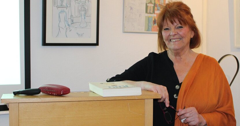 Suzanne Bohn bei ihrem Vortrag im letzten Jahr. Suzanne Bohn lehnt sich gegen ein Stehpult, im Hintergrund sind gerahmte Bilder zu sehen. Das Foto entstand letztes Jahr in der Kunstgalerie am Büchnerhaus.