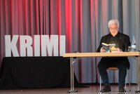 Michael Kibler sitzt an einem Tisch mit einem Buch von ihm und liest daraus vor