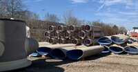 Auf einem Lagerplatz liegen mehrere Kanalrohre auf dem Boden. Sie sind nicht rund, sondern oval und laufen unten spitz zu. Innen sind sie blau ausgekleidet. Im Hintergrund sind normale runde Kanalrohre übereinander gestapelt.