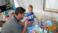 Ein Vater sitzt mit seinem Sohn an einem Basteltisch.