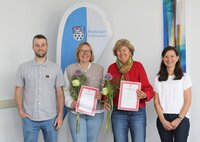 Fachbereichsleiter Rick Hölzer und Fachberaterin Nadja Pfitzner umrahmen die erfolgreichen Absolventinnen Anja Ohl und Anja Fehr (v.li.) Vor einer blau-weißen Fahne mit dem Wappen und der Aufschrift Büchnerstadt Riedstadt stehen Fachberichsleiter Rick Hölzer, die erfolgreichen Absolventinnen Anja Ohl und Anja Fehr sowie Fachberaterin Nadja Pfitzner. Ohl und Fehr halten ihre Zertifikate in den Händen.