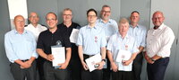 Die geehrten Feuerwehrleute stehen in schwarzer oder hellblauer Dienstkleidung in einer Reihe und halten ihre Urkunden in den Händen. Umgeben sind sie vom stellvertretenden Stadtbrandinspektir Peter Wendel, Kreisbrandinspektor Friedrich Schmidt, Stadtbrandinspektor Markus Kölsch sowie Bürgermeister Marcus Kretschmann