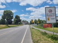 Schilder weisen ausdrücklich auf das Durchfahrtverbot und die Umleitungsstrecke für Lkws hin. Links im Bild ist die Landstraße zu sehen, die durch Leeheim führt, im Hintergrund ist der Ortsanfang. Rechts im Bild zeigen Schilder das Durchfahrtverbot für Lkw und den Pfeil der Umleitungsstrecke.