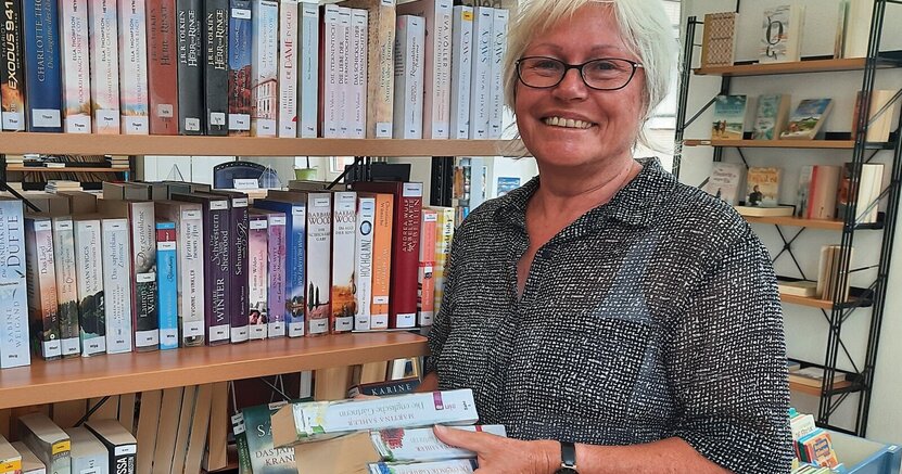 Bärbel Schmidt steht in der Bücherei Leeheim zwischen Bücherregalen und hält einen Stapel Bücher in der Hand.