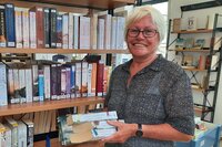 Bärbel Schmidt steht in der Bücherei Leeheim zwischen Bücherregalen und hält einen Stapel Bücher in der Hand.