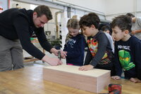 Auch gehämmert wurde mit Hilfe der Profis. André Lindemann hilft Annabelle, einen Nagel in den Holzkasten zu hämmern. Emilio und Eymen schauen zu.