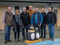 Klaus und Ruth Trapp und Karl-Heinz Kopp (vom Schwimmbadverein) sowie Peter Philipp, Christian Lorenz, Michael Klosterhalfen, Marc Gaillard (vom Linux-Café) stehen am Rand des Schwimmbeckens im Freibad Crumstadt. Vor ihnen stehen zwei Wasserspeier in Form von Pinguinen.