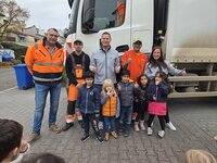 Kinder und Erwachsene stehen vor einem Müllauto