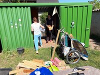 Emsig aufgeräumt wurde beim Garten-Fit-Tag der Kita Sonnenschein. Vor einem grünen Container auf dem Außengelände der Kita Sonnenschein liegen und stehen unter anderem verschiedene Bretter und ein Fahrradanhänger für Kinder.