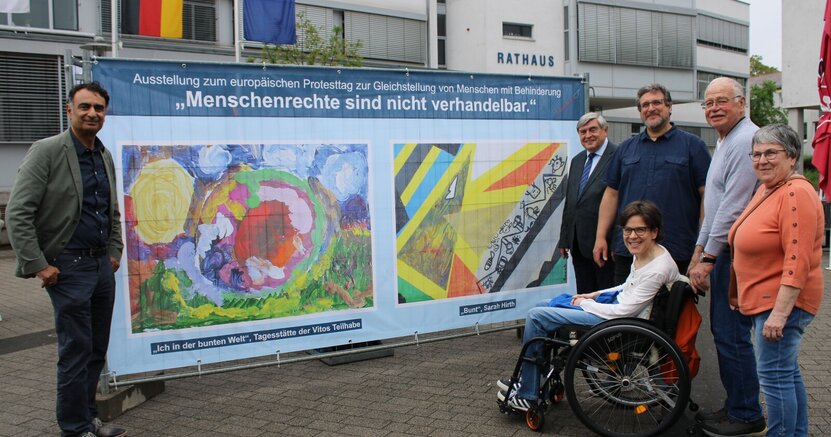 Erster Kreisbeigeordneter Adil Oyan, Erster Stadtrat Richard Kraft, Kulturbüroleiter Marco Hardy, Behindertenbeauftragte Marina Wohner sowie ihre Eltern Horst und Hannelore Wohner (v.li.) bei der Ausstellungseröffnung. Auf dem Rathausplatz stehen vor einem großen Banner mit zwei bunten Gemälden der Erste Kreisbeigeordneter Adil Oyan, Erster Stadtrat Richard Kraft, Kulturbüroleiter Marco Hardy, Behindertenbeauftragte Marina Wohner sowie ihre Eltern Horst und Hannelore Wohner (v.li.)
