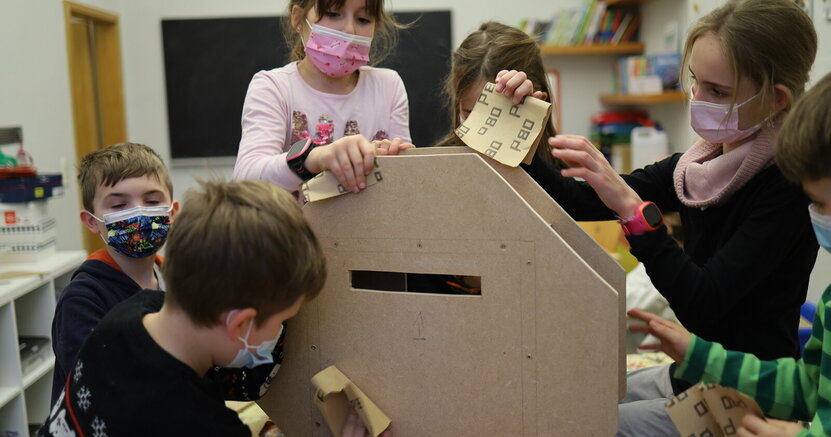 Mehrere Kinder mit Maske schmirgeln an einem großen Holzstück.