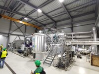 In einer Halle steht im Vordergrund ein Mensch mit grünem Helm. Im Hintergrund sind die silberfarbenen Bauten der Flußwärmepumpe Mannheim zu sehen.