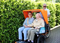 Ulrike Röder und ihre Mutter Elfriede Behrendt sitzen vorne in der Rikscha. Hintern ihnen sitzt Fahrer Horst Geißler auf dem Fahrradsitz.