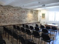 In der Kunstgalerie am Büchnerhaus stehen Stuhlreihen vor einem Tisch. Die rückwärtige Längswand besteht aus großen alten Steinen.