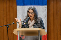 Géraldine Beltramelli steht an einem Rednerpult mit Mikrofon, hinter ihr ist ein Teil der französischen Flagge zu sehen.