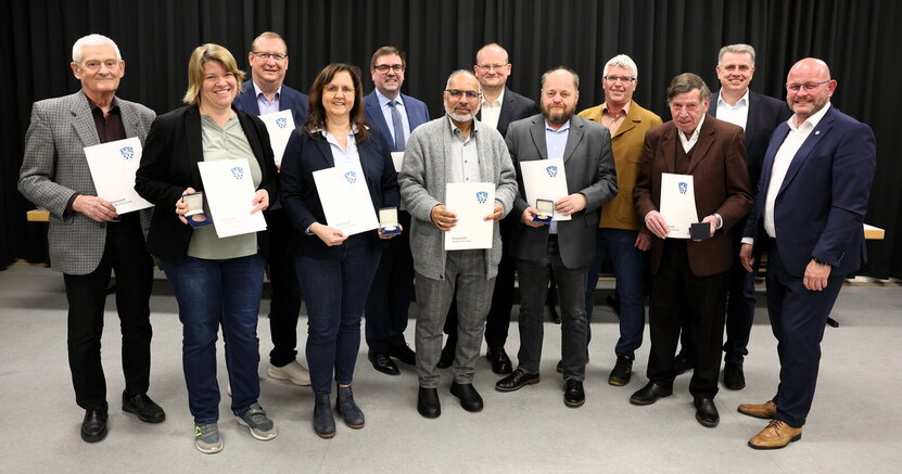 Auf der Bühne der Heinrich-Bonn-Halle stehen die Ausgezeichneten mit Ehrenplaketten und Urkunden. Von links nach rechts:Dieter Frey, Katja Kamenik, Matthias Lachmann, Melanie Dörr, Guido Funk, Ahmad Muzaffar Mahmood, Michael Fraikin, Matthias Thurn, Ottmar Eberling, Frank Fischer, Heiko Büßer und Bürgermeister Marcus Kretschmann 
