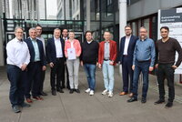 Vor dem Landratsamt stehen v.l.n.r. die Bürgermeister Thomas Raschel (Stockstadt am Rhein), Marcus Merkel (Büttelborn), Jörg Rüddenklau (Groß-Gerau), Peter Burger (Gernsheim) und Marcus Rahner (Biebesheim am Rhein), Marion Götz (Leiterin IKZ-Lenkungsgruppe), Bürgermeister Marc Friedrich (Nauheim), Landrat Thomas Will, die Bürgermeister Karsten Groß (Mörfelden-Walldorf) und Thorsten Siehr (Ginsheim-Gustavsburg) sowie Erster Kreisbeigeordneter Adil Oyan. Marion Götz hält den Förderbescheid in der Hand.