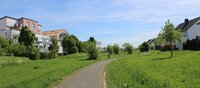 Links und rechts eines Fußweges sind Wiesen und Bäume einer Parkanlage zu sehen, dahinter kommen auf beiden Seiten Häuser des Quartiers "Am Hohen Weg".