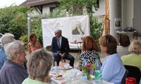 Eine Frau und ein Mann sitzen auf Stühlen vor den Besuchern des Sommerfestes. Der Mann trägt eine Schiebermütze. Sie spielen einen Sketch.