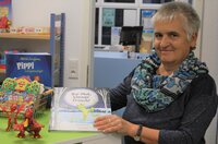Büchereimitarbeiterin Ellen Stieb steht am Empfang der Bücherei Wolfskehlen und hält ein Bilderbuch in der Hand.