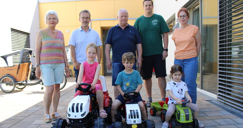 Die Traktorfahrer Adelina, Giosuè und Tiana (v.li.) mit Ute Nold-Stenzel, Michael Klosterhalfen und Günter Kleinwächter vom Reparaturcafé sowie dem stellvertretenden Kitaleiter Nico Gade und Kitaleiterin Carolin Brückmann. Vor der Kita Am Park sitzt Adelina auf dem größten Trettraktor, daneben Giosuè auf einem mittelgroßen Traktor und Tiana auf dem kleinsten Traktor. Dahinter stehen Ute Nold-Stenzel, Michael Klosterhalfen und Günter Kleinwächter vom Reparaturcafé sowie dem stellvertretenden Kitaleiter Nico Gade und Kitaleiterin Carolin Brückmann.