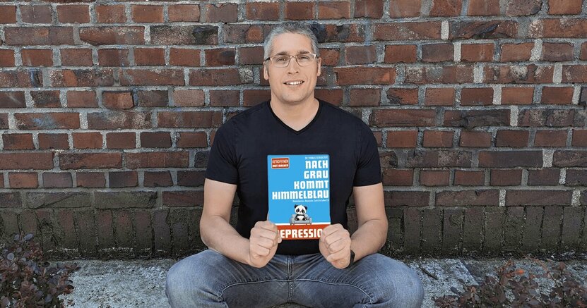 Autor Thomas Reinbacher hält sein Buch in der Hand.