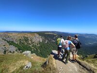 Jugendliche genießen den Ausblick bei einer Wandertour. Drei Jugendliche stehen auf einem Berg und schauen auf die Berglandschaft und den blauen Himmel.