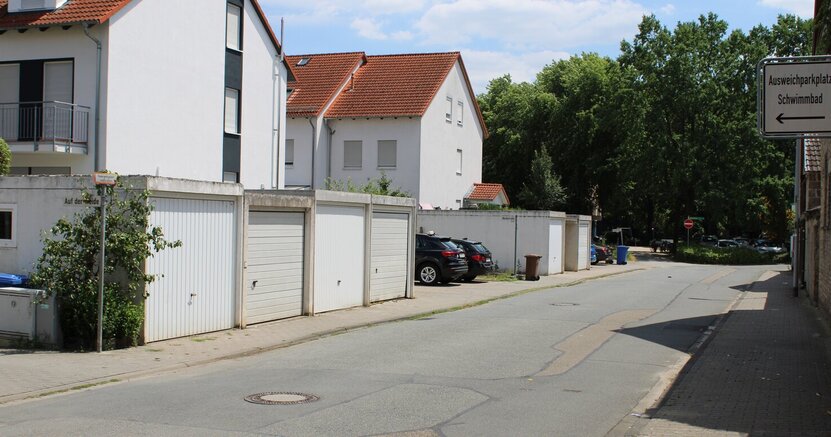 Ein Schild in der Weidstraße weist auf den Ausweichparkplatz hin. Das Foto zeigt die Weidstraße in Goddelau. Im Hintergrund sind die Bäume vor dem Freibad Goddelau zu sehen. Im Vordergrund zeigt vorne rechts ein Schild den Weg zum Ausweichparkplatz für das Freibad Goddelau.