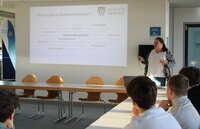 Julia Galley gab einen Überblick über die Aufgaben einer Stadtverwaltung. Julia Galley steht vor einer Wand im Sitzungssaal. Neben ihr wird eine Präsentation zu den Aufgaben der Stadtverwaltung an der Wand abgebildet.